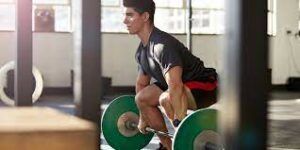 A man is squatting down with a barbell in a gym.