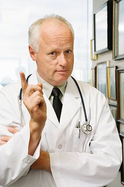 A doctor with a stethoscope around his neck is giving a thumbs up.