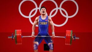 A man is lifting a barbell in front of the olympic rings.
