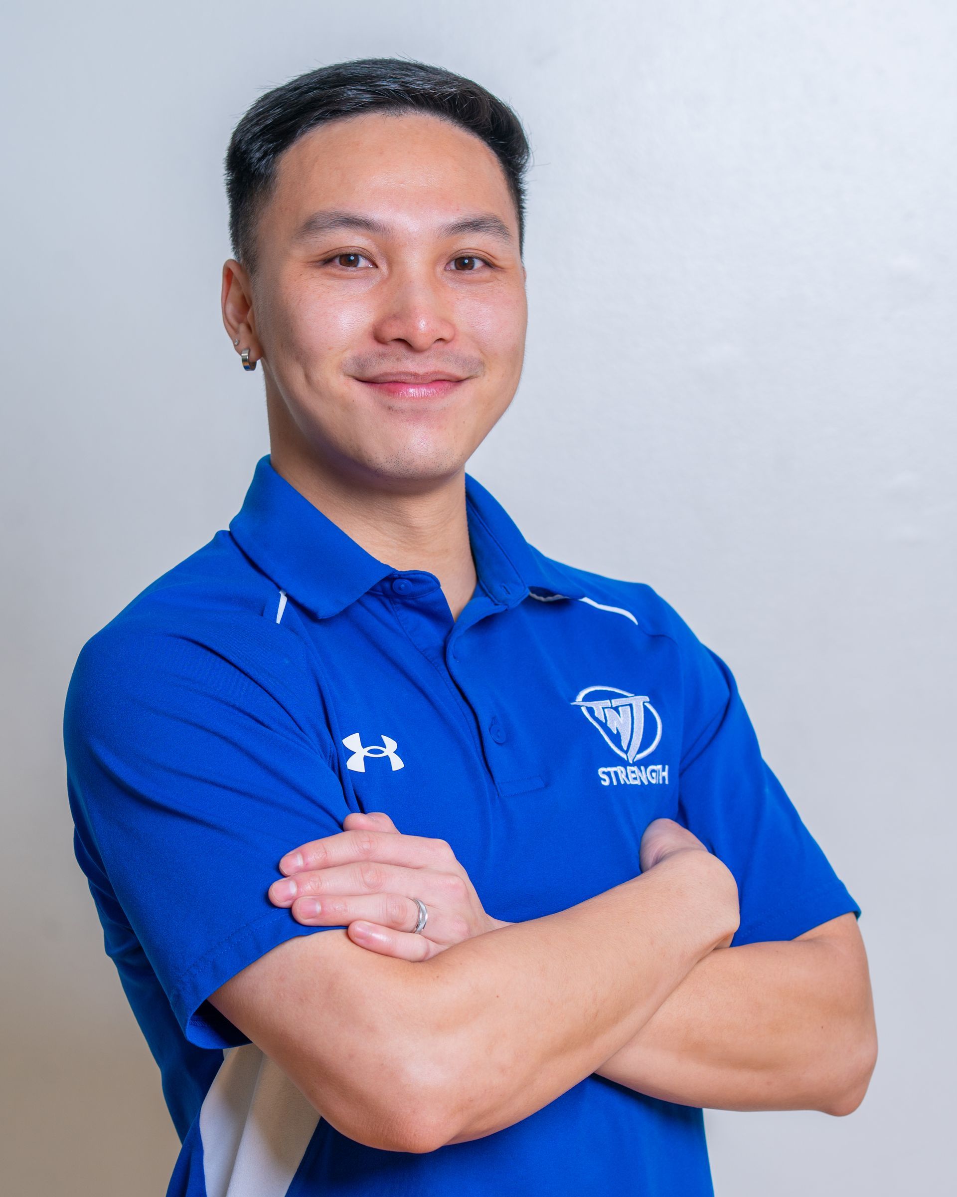 A young man in a blue shirt is standing with his arms crossed.