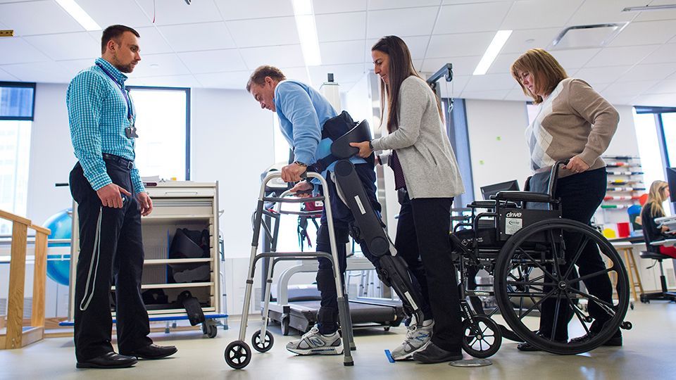A group of people are standing around a man in a walker and a woman in a wheelchair.