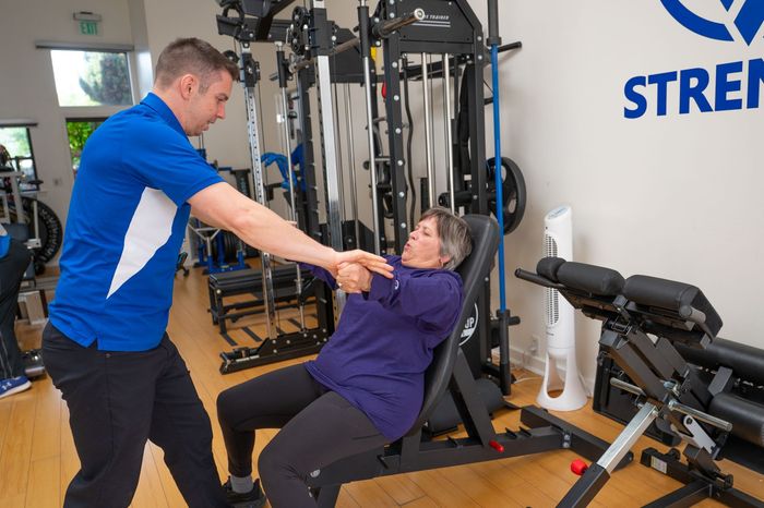 Trainer assisting client with seated exercise in a gym, near weight machines and equipment