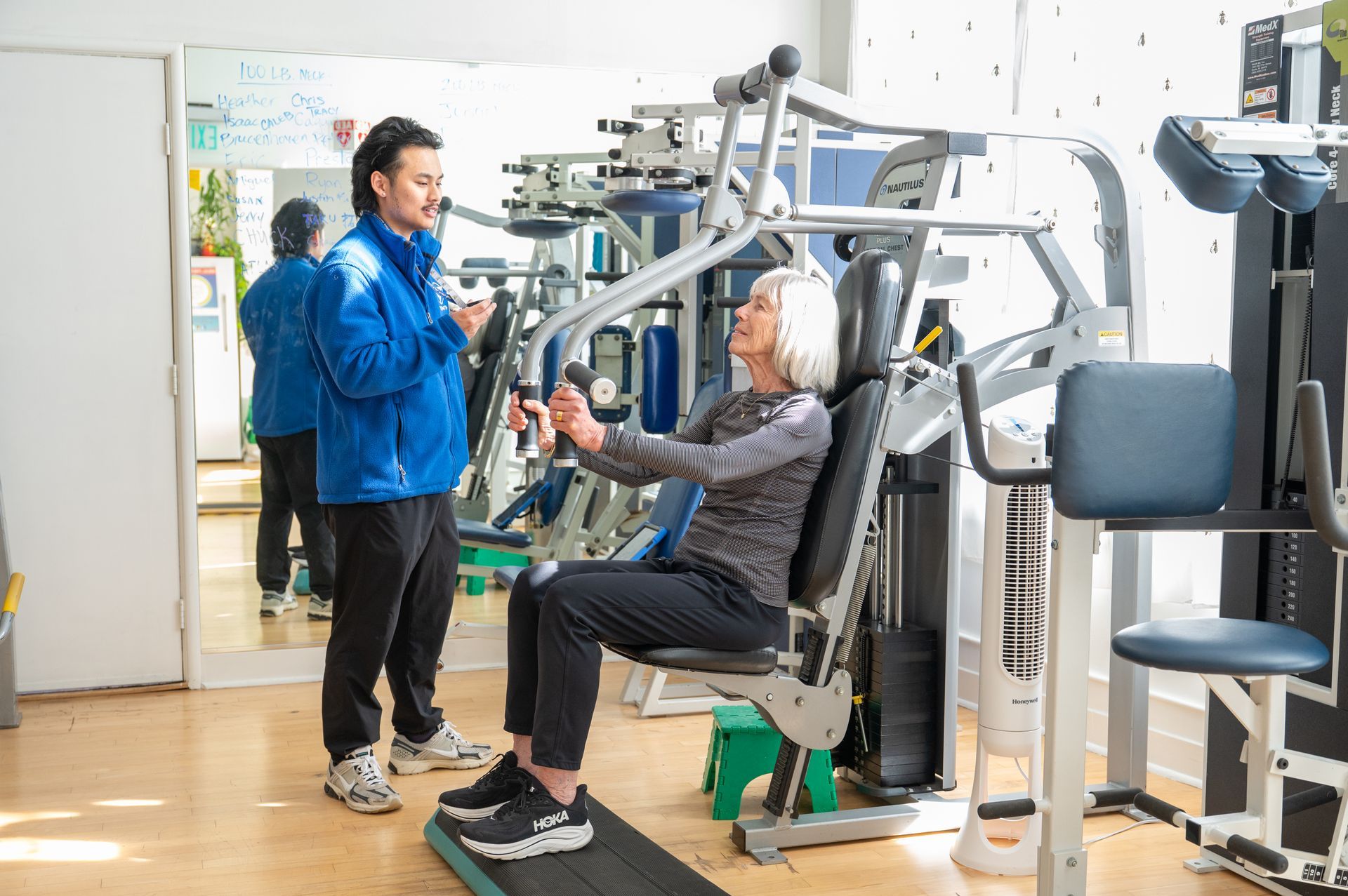 Trainer assisting seated woman with exercise machine in a gym