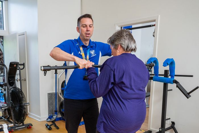 Therapist assisting a client with exercise in a rehab gym, using a parallel bar for support