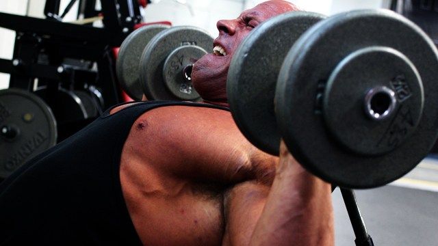 A man is lifting dumbbells on a bench in a gym