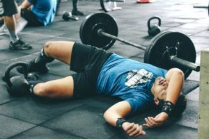 A man is laying on the floor in a gym with a barbell.