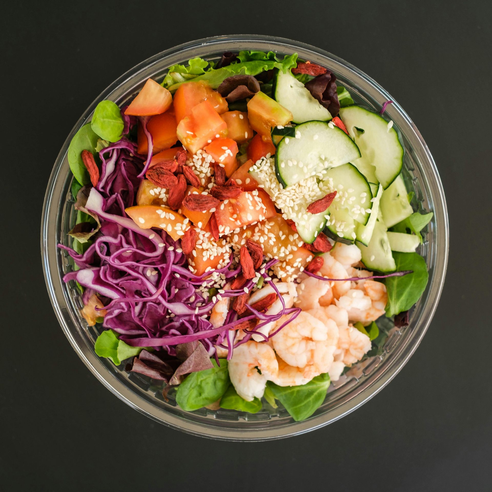 Colorful salad bowl with cucumbers, purple cabbage, greens, tomatoes, shrimp, and dressing