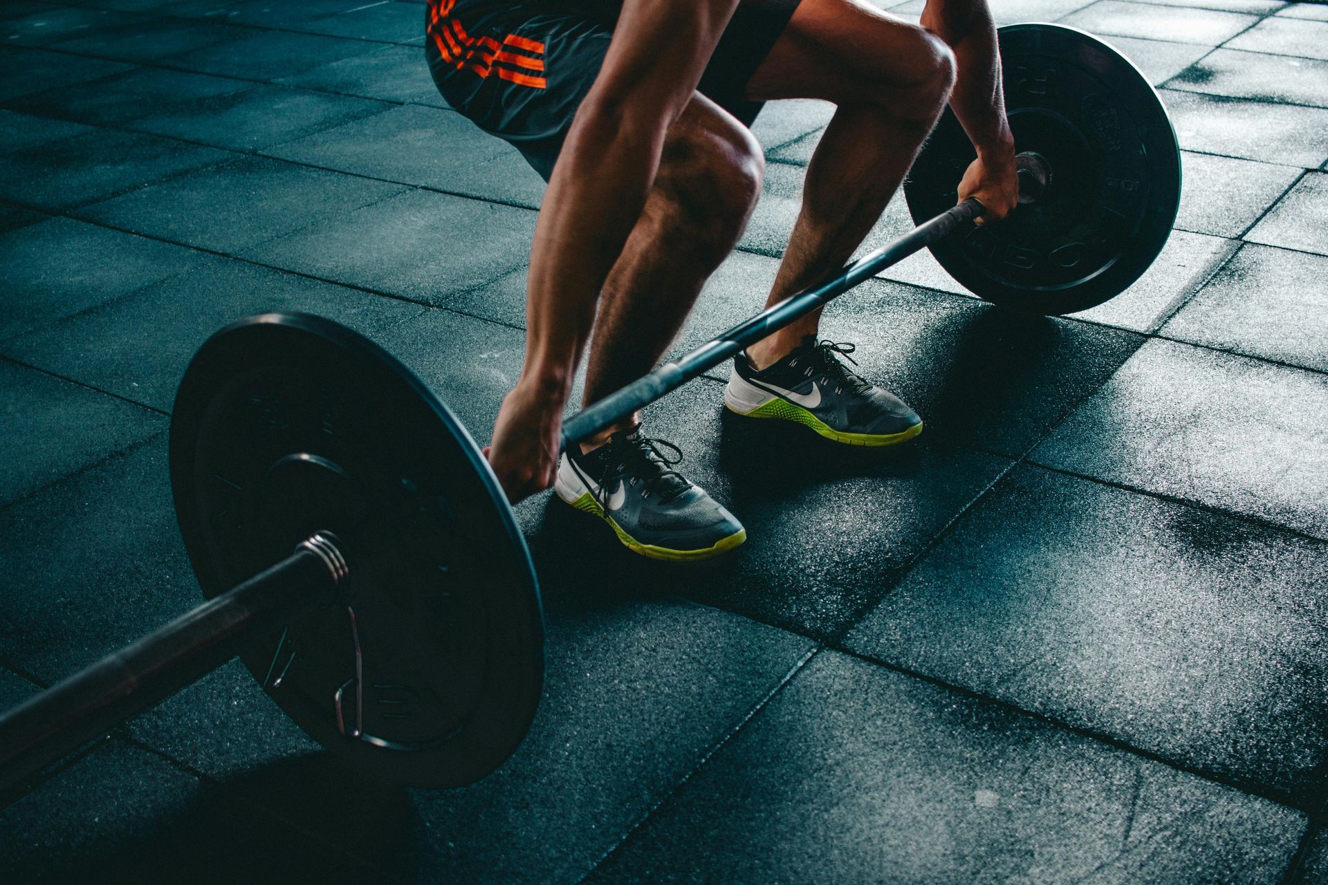Athlete lifting a barbell on a gym floor, wearing neon green shoes under moody lighting