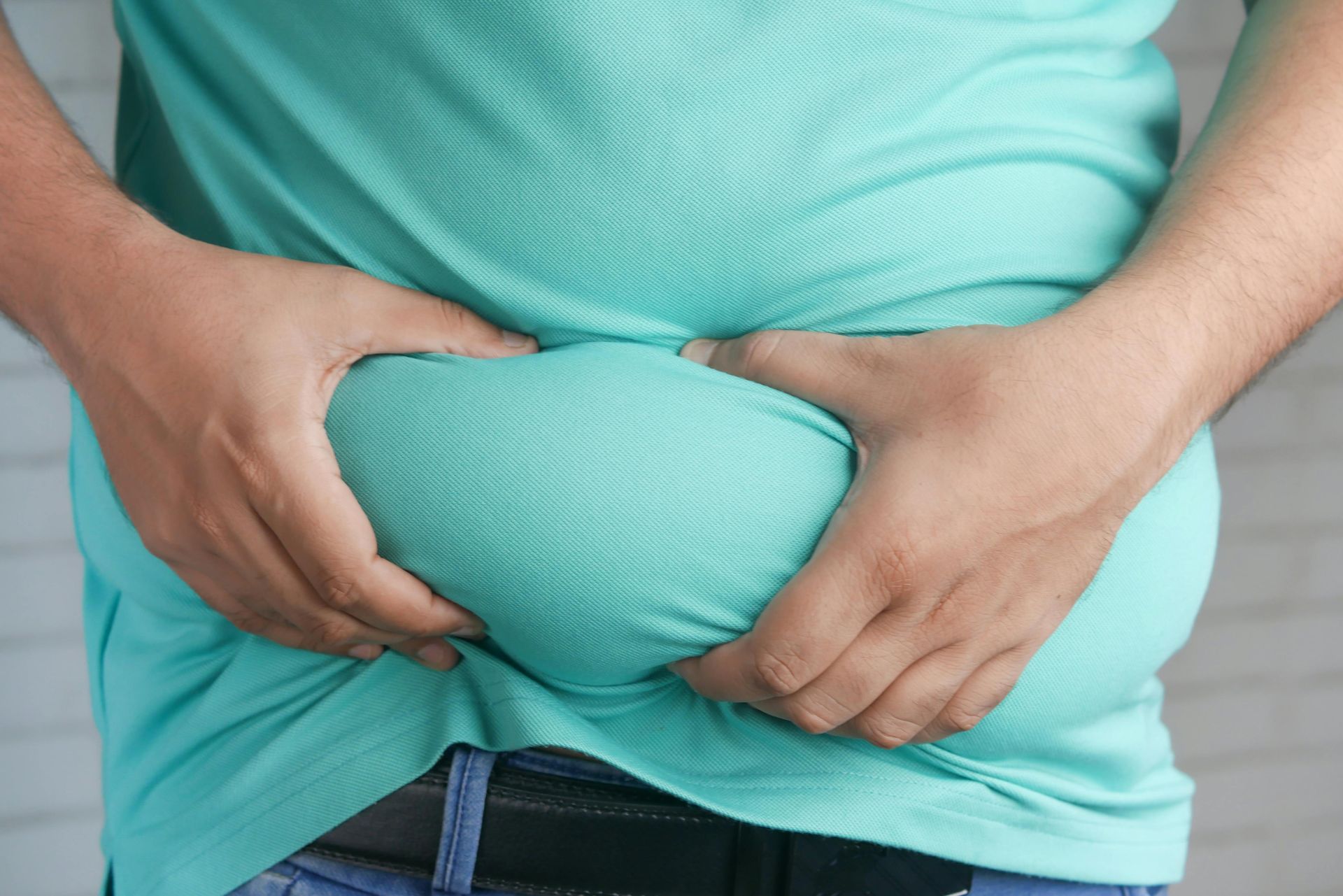 Hands gripping a turquoise shirt tightly over a rounded belly.