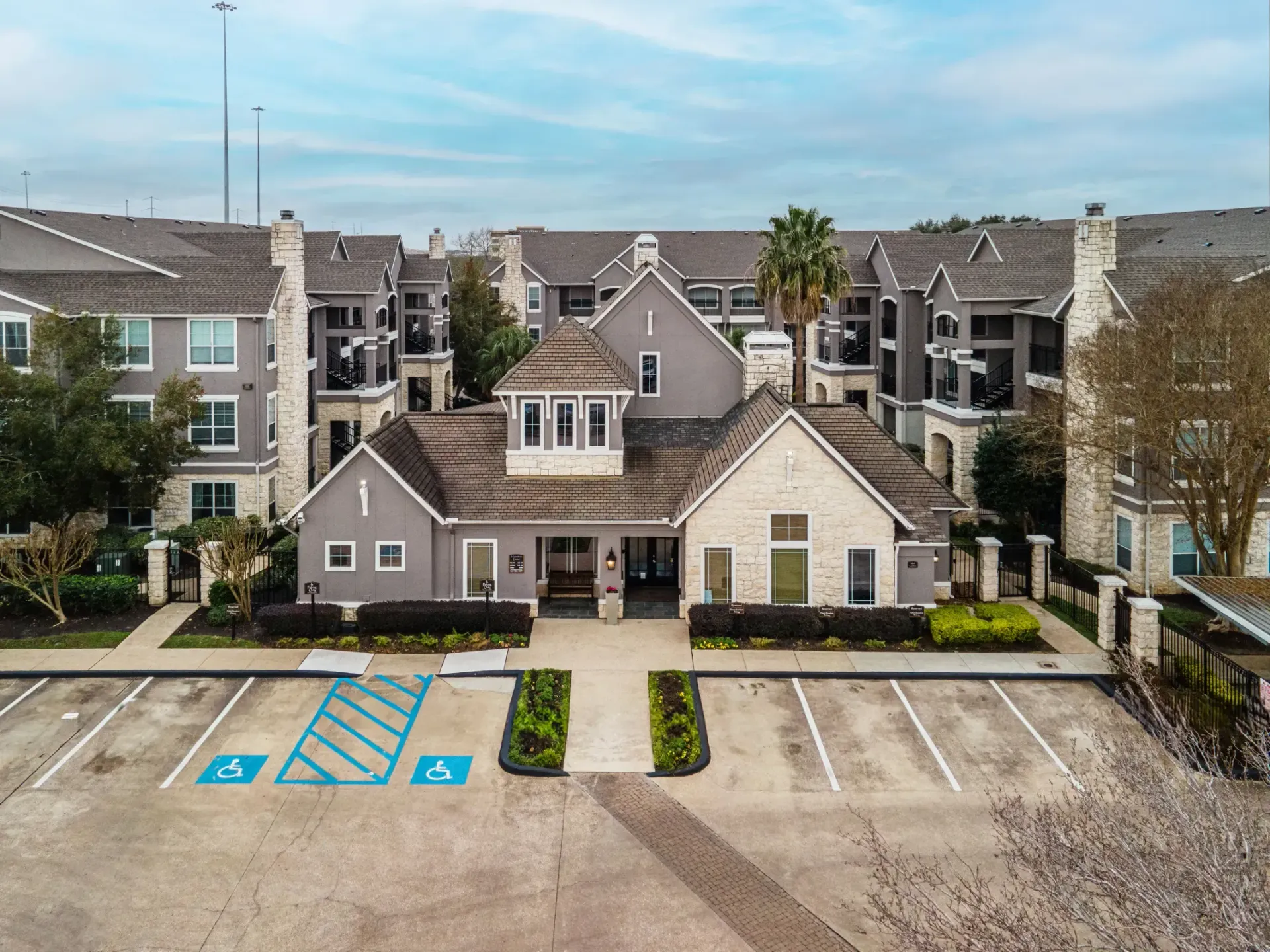 Apartment complex with a central, stone-clad clubhouse and surrounding multi-story buildings; parking lot in front.