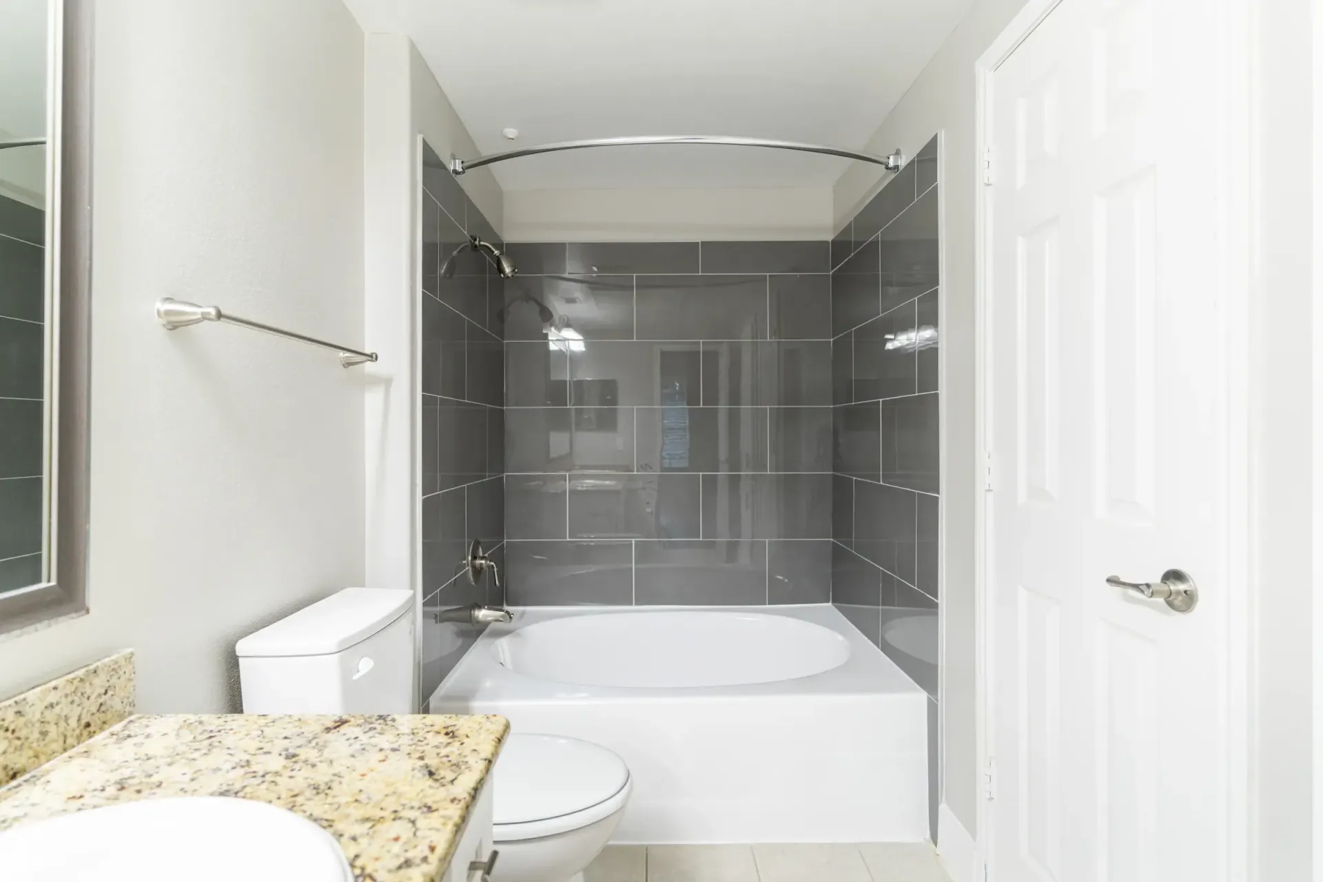 Bathroom with a white bathtub, gray tiled walls, a toilet, and a vanity.