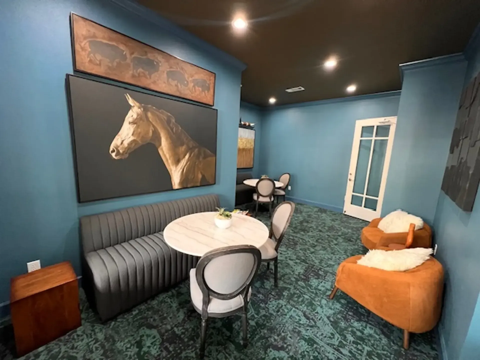 Interior of a room with a seating area, a round table, and a horse portrait. Turquoise walls and a dark ceiling.