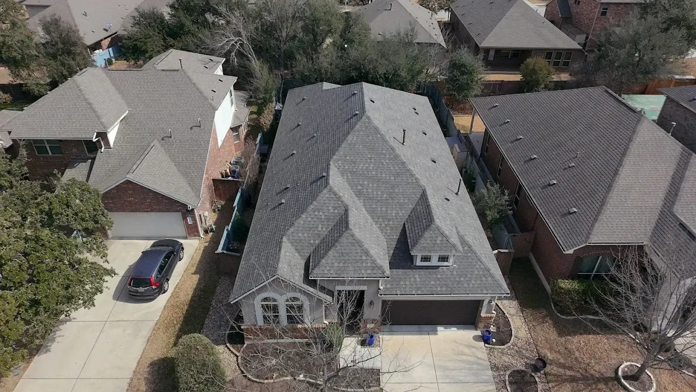 Aerial view of a suburban house with a gray roof, driveway, and neighboring homes