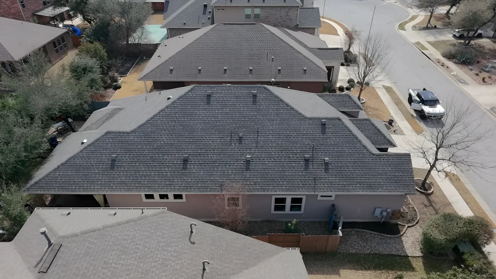 Aerial view of suburban homes with gray roofs and a street with parked cars.