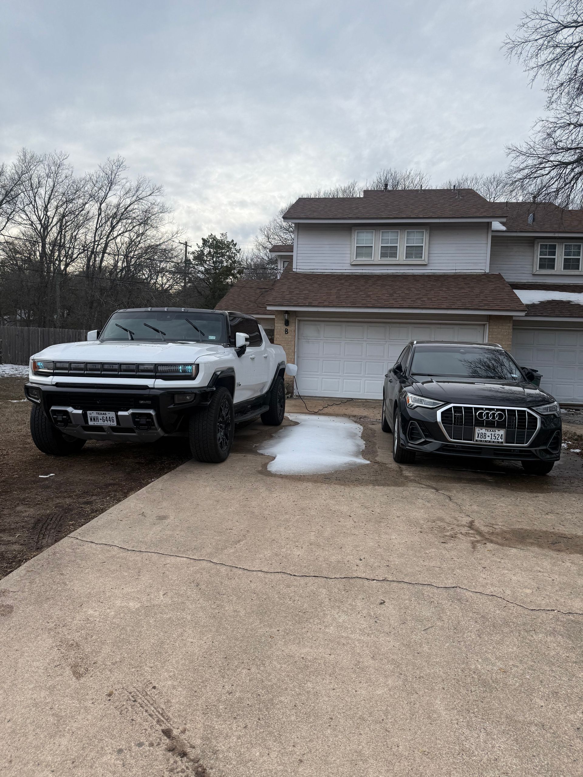 Two SUVs parked in a driveway in front of a two-story house, with patches of snow on the ground.