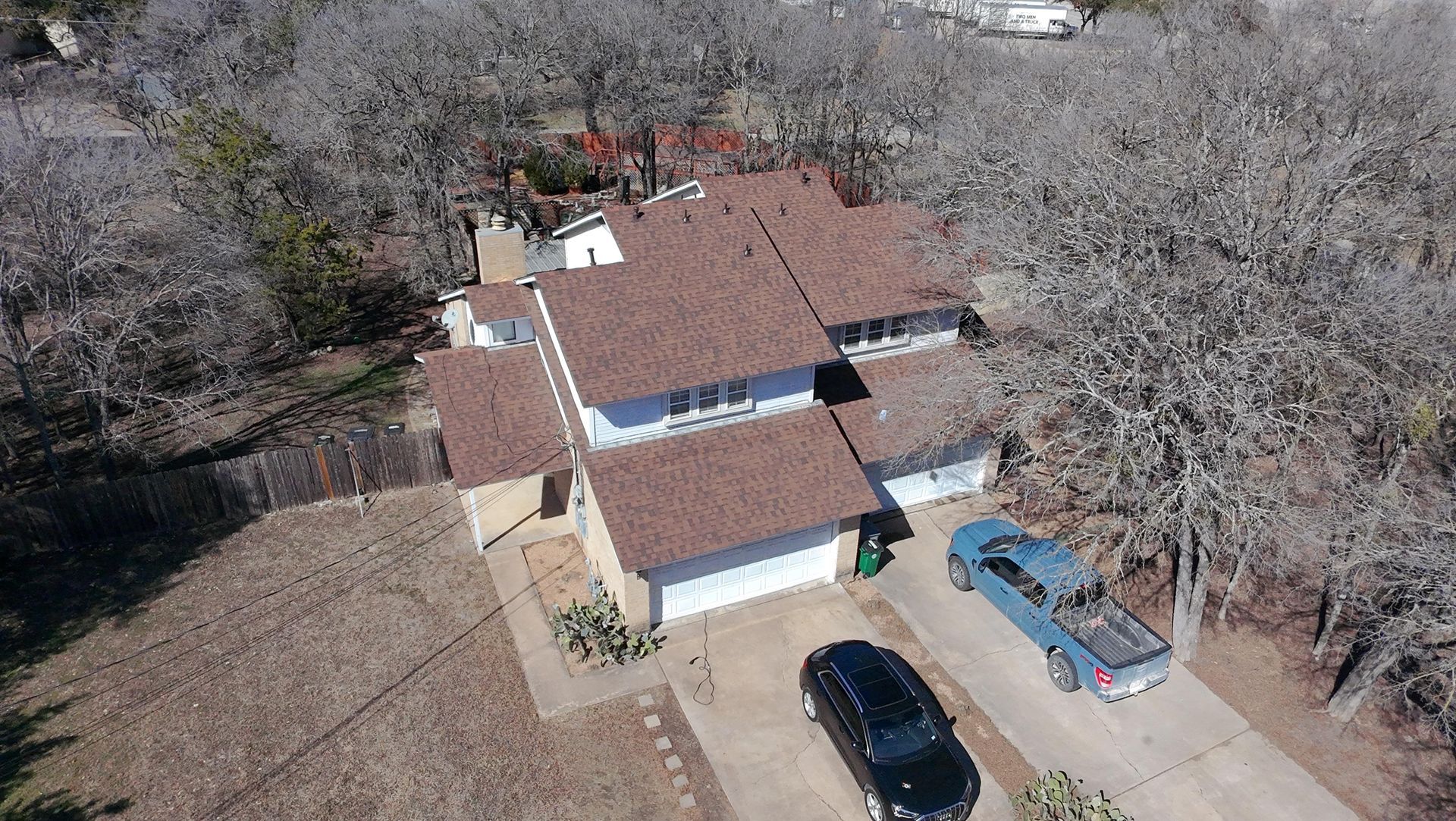 Aerial view of a two-story house with a red roof and three cars parked in the driveway, surrounded by trees.