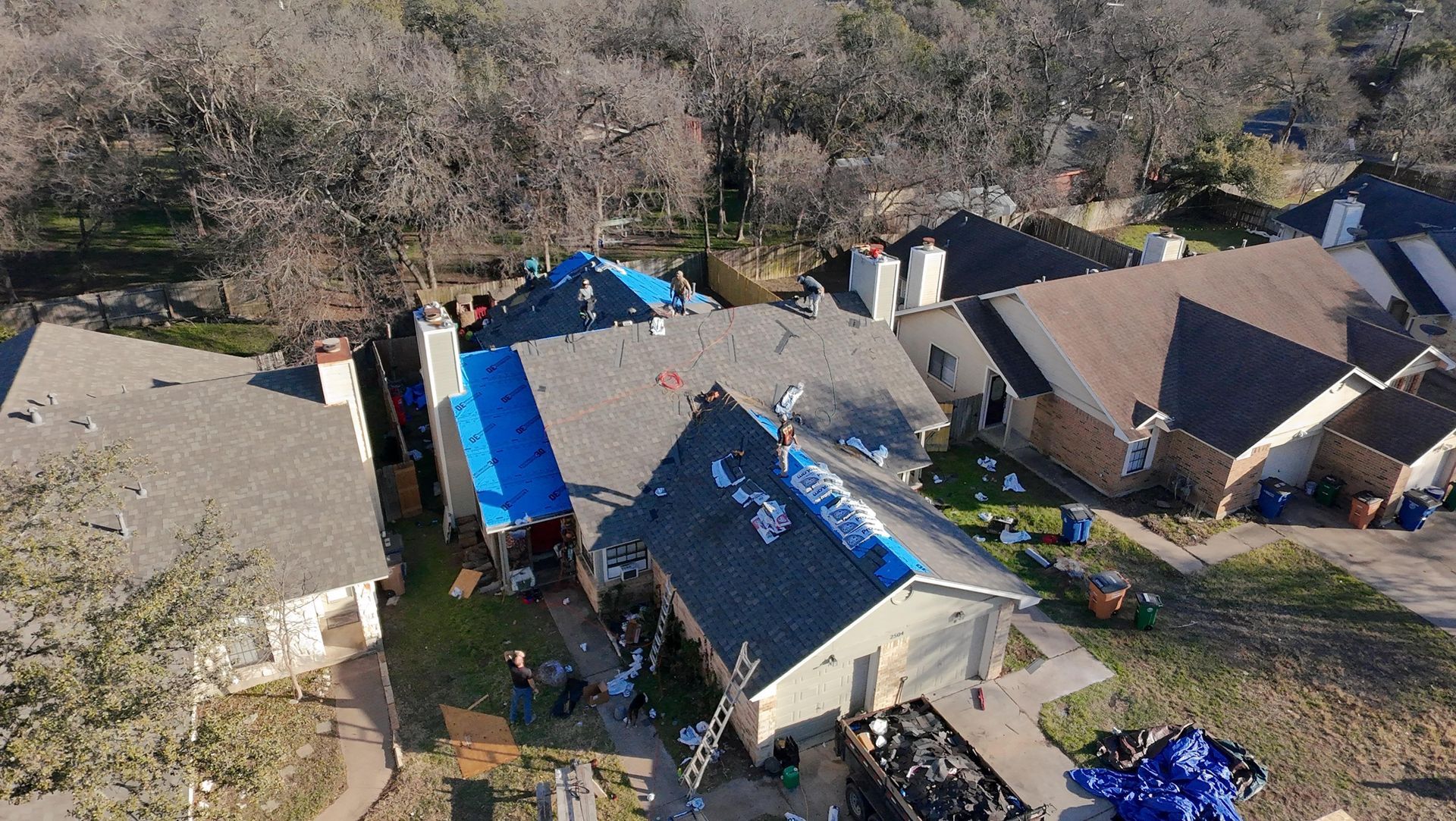 Aerial view of storm-damaged houses with blue tarps covering rooftops in a residential area