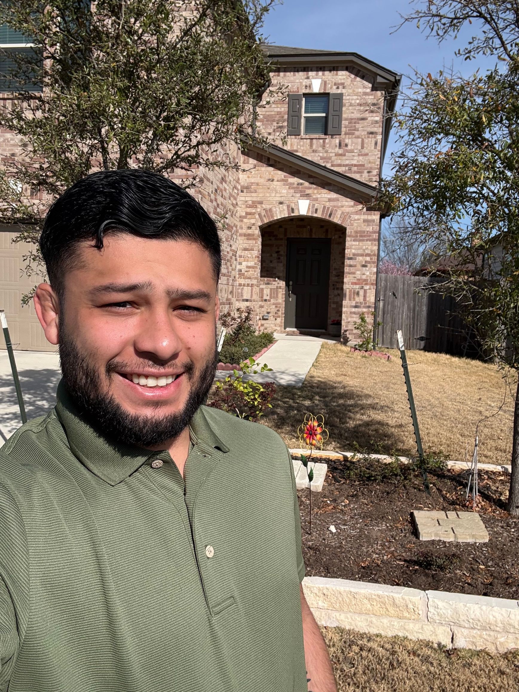 Man taking a selfie in front of a brick house on a sunny day