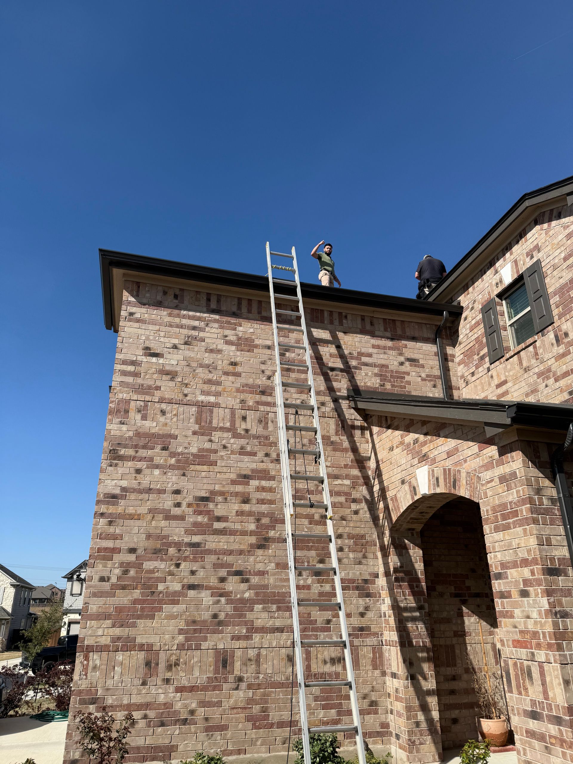 Two people on a ladder repairing a brick building under a clear blue sky