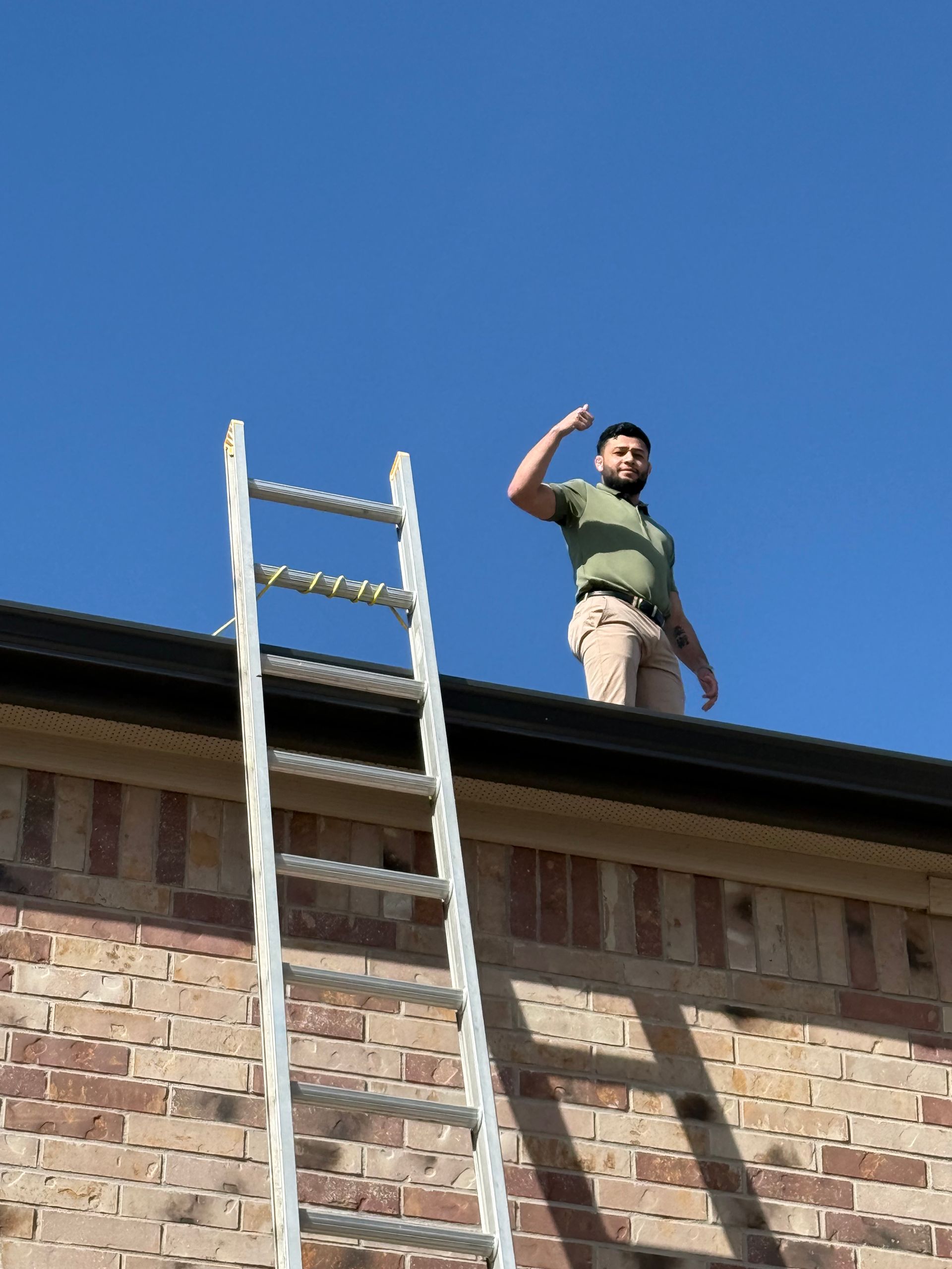 Person standing on a rooftop beside a ladder, waving against a clear blue sky.