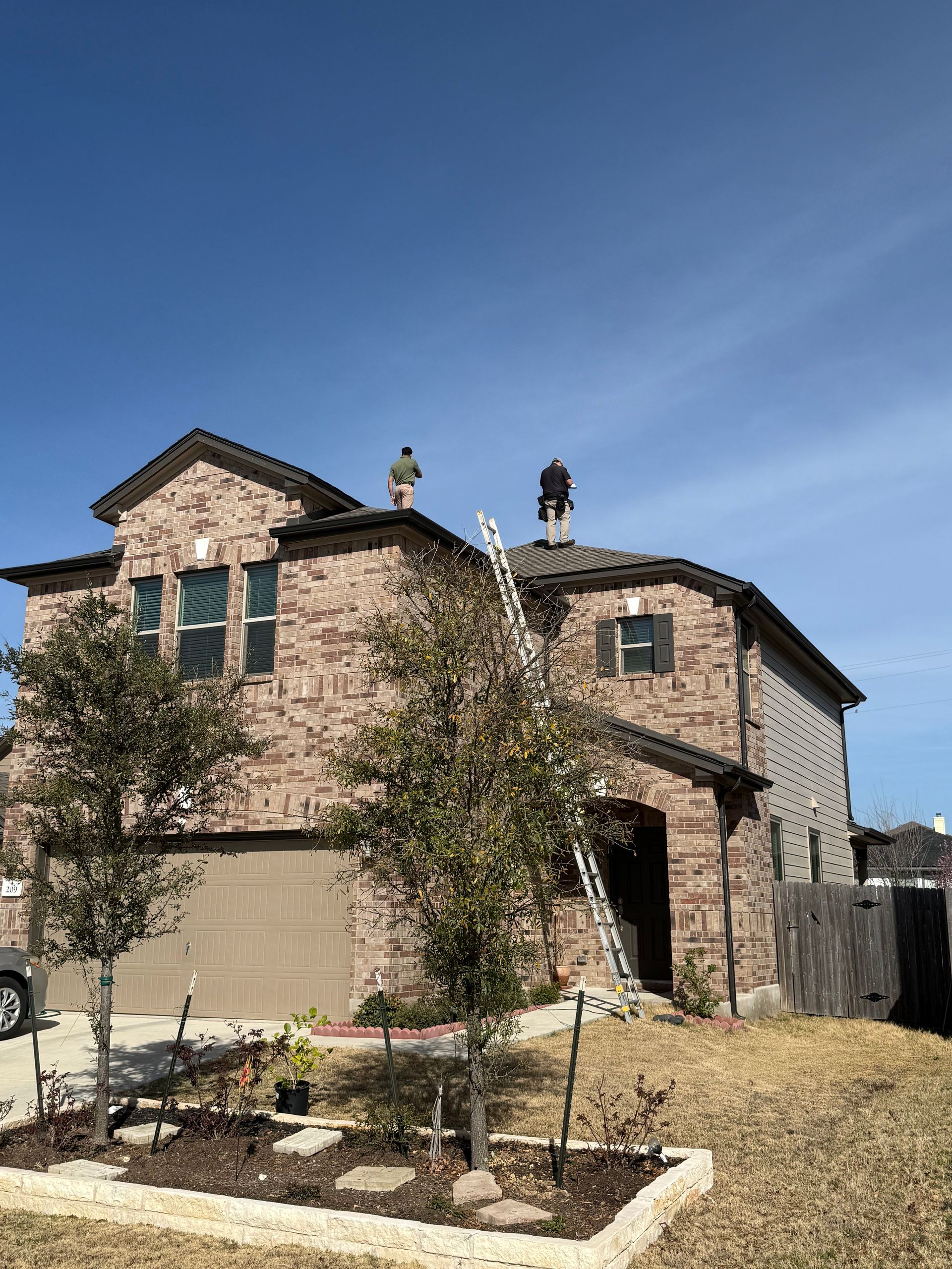 Stone house with arched entry, green shutters, and young trees under a clear blue sky
