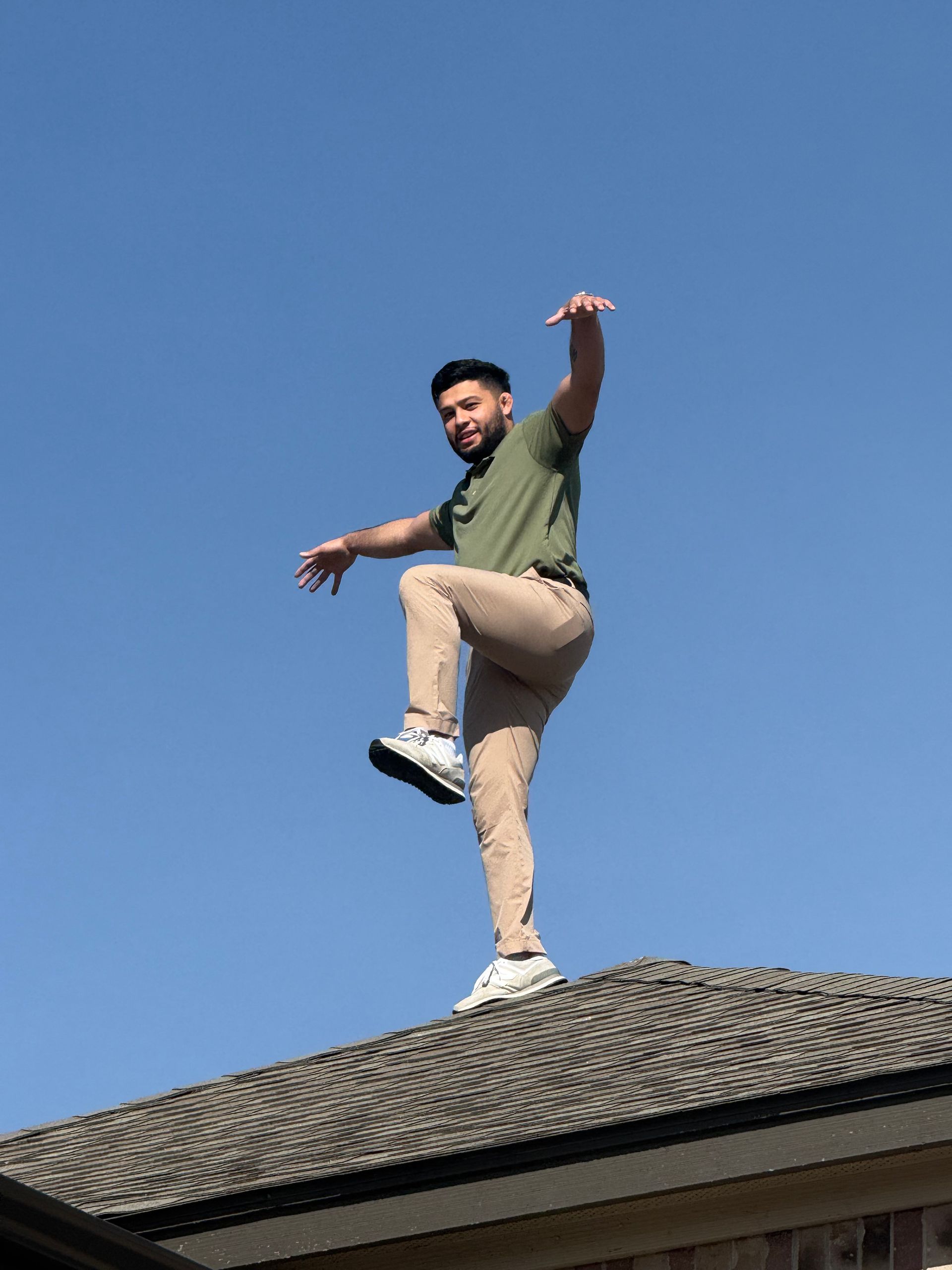 Man balancing on one leg atop a roof against a clear blue sky