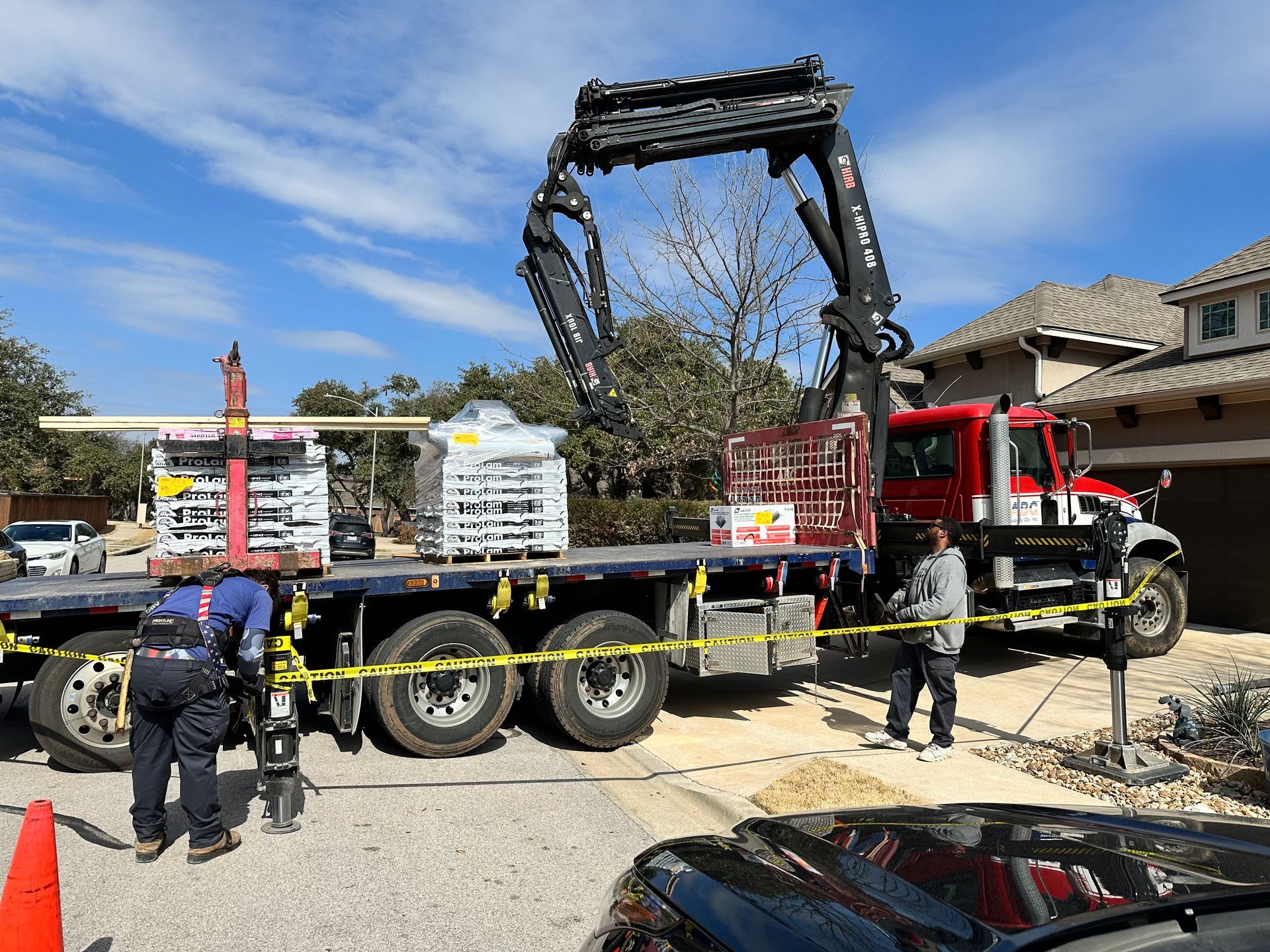 Workers beside a red logging truck unloading a large black metal frame at a gravel site