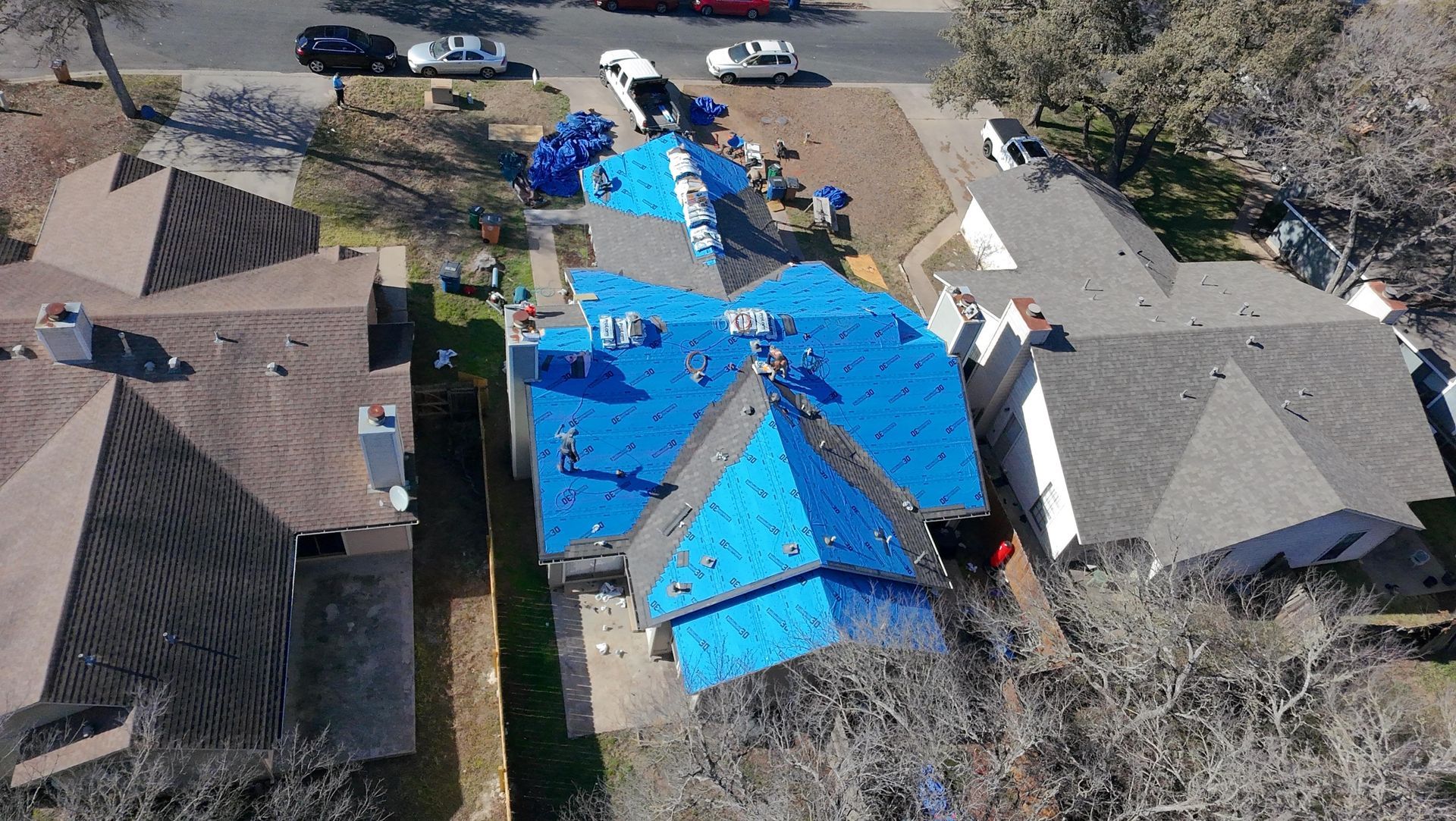 Aerial view of a house with a bright blue tarp covering the roof after storm damage.