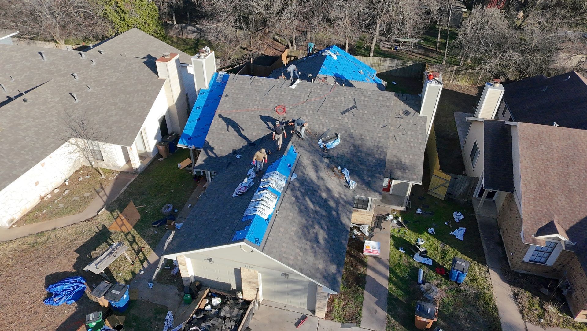 Aerial view of a damaged house roof covered with blue tarps after storm repair