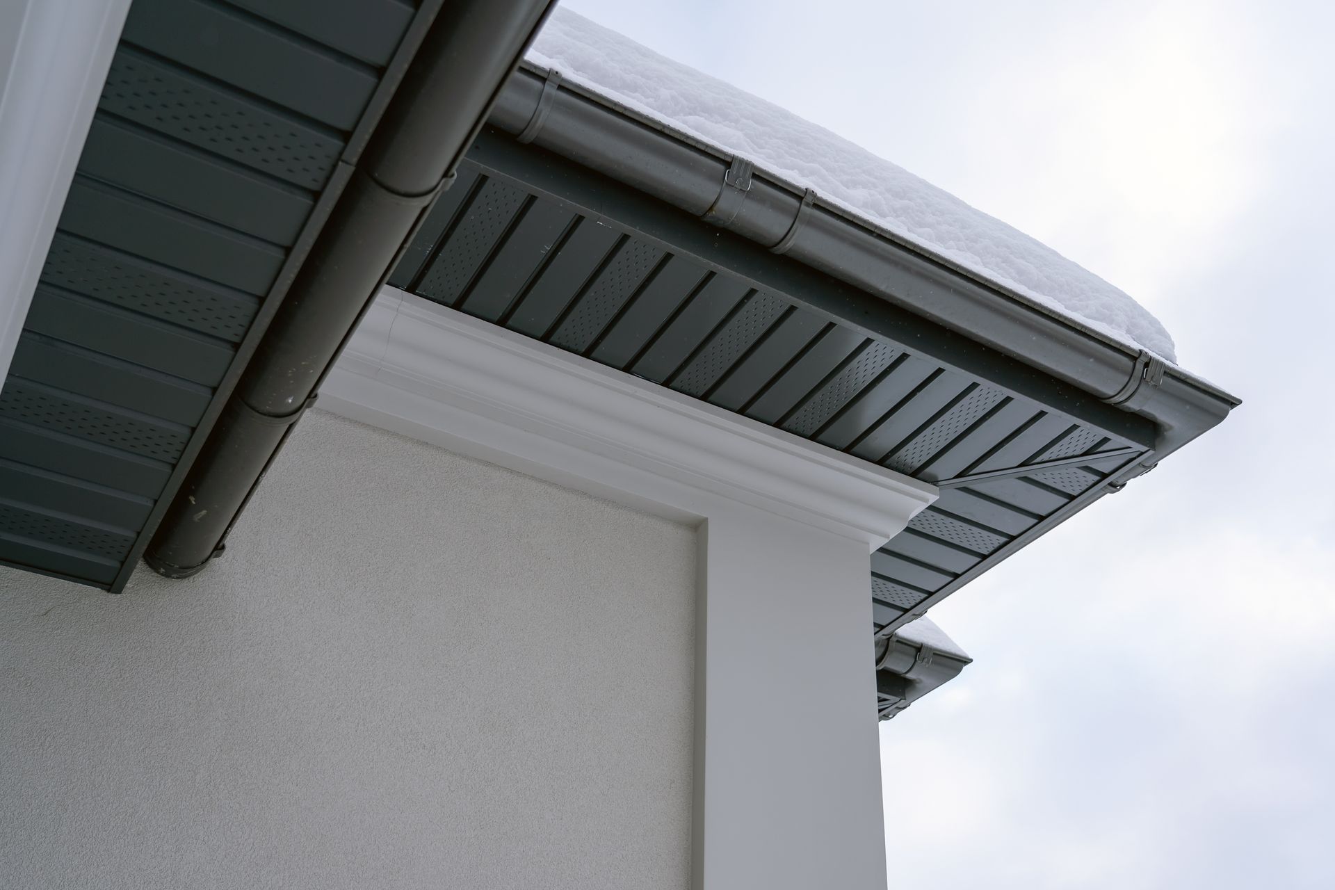 Close-up of a house roof eave with gray soffit and gutter against a bright sky