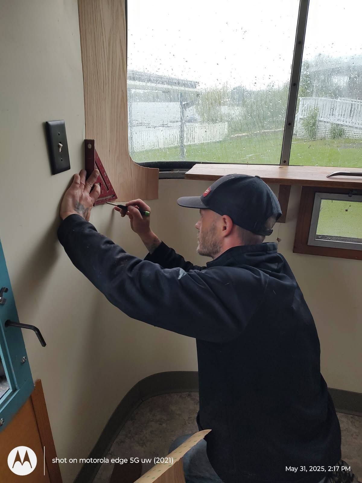 Man hanging a red curtain bracket in a room beside a window with rain outside.