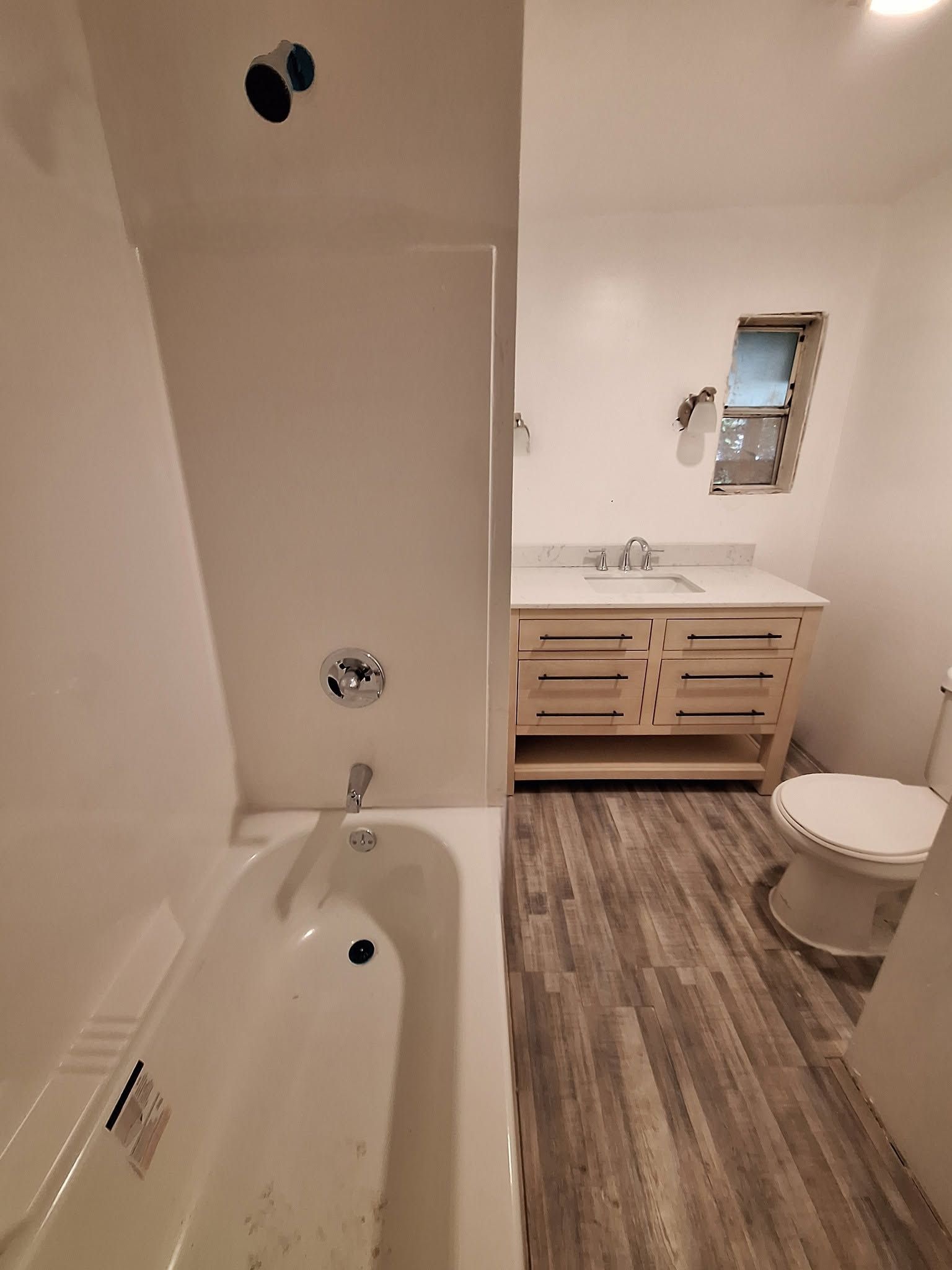Bathroom with a bathtub on the left and a wood vanity, sink, and toilet on the right.