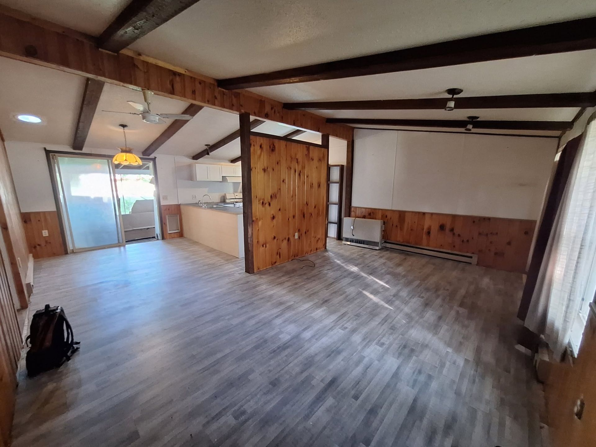 Empty rustic living room with wood beams, gray floor, and sliding glass doors to a patio.