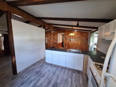 Small rustic kitchen with white cabinets, wood-paneled wall, and gray flooring