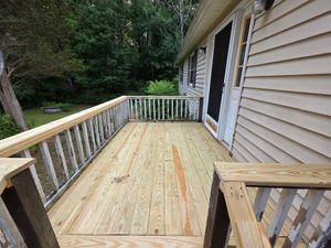Wooden deck under construction beside a beige house, with white railing and wooded yard.