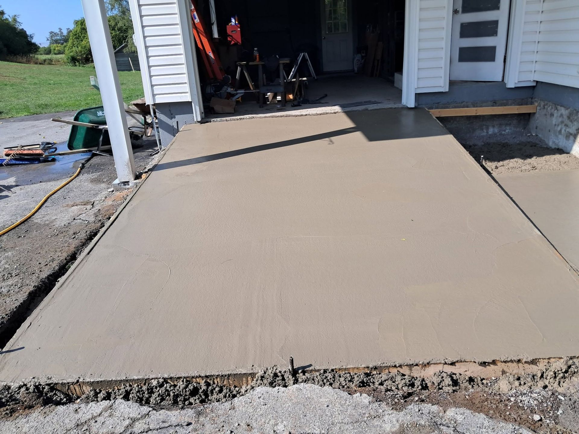 Freshly poured concrete ramp leading into a garage beside a white house