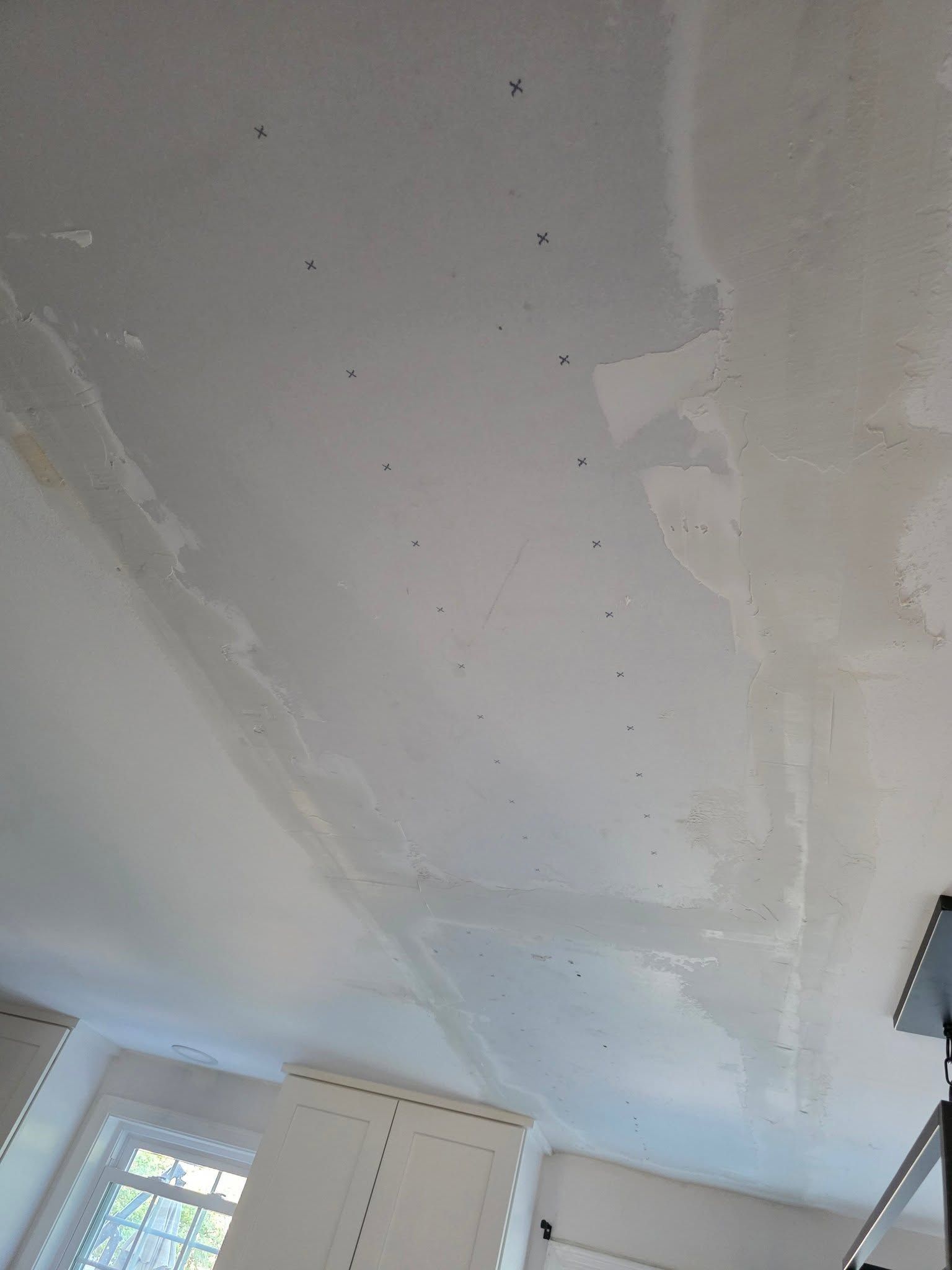 White room ceiling with patches of drywall repair and a window below