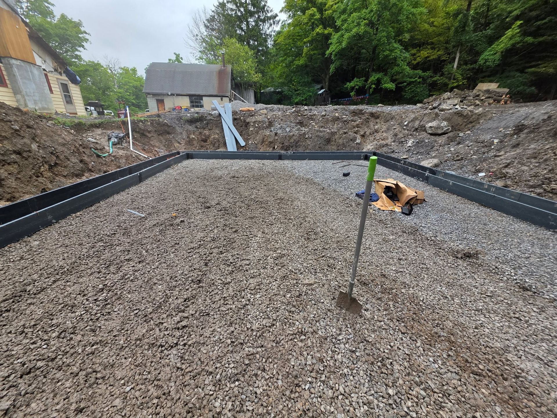 Gravel foundation for a house under construction, with black edging and trees in the background.