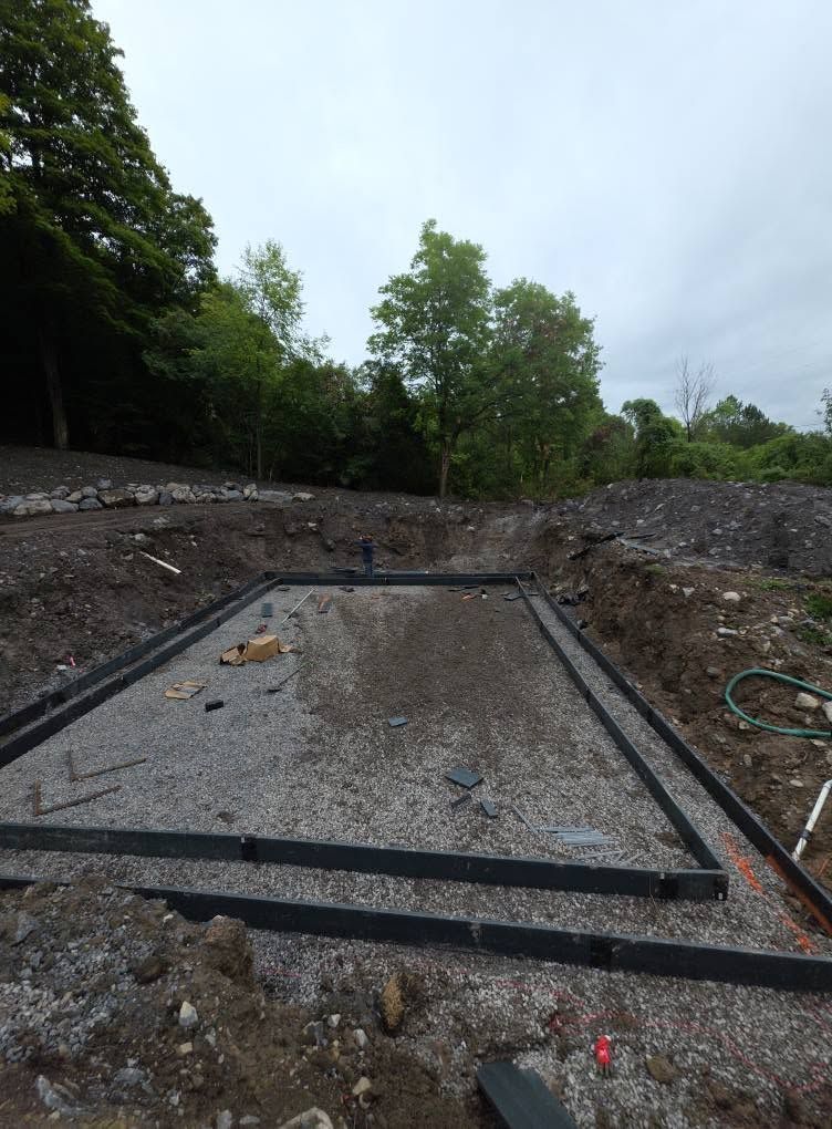 Concrete foundation pit surrounded by dirt and trees at an outdoor construction site