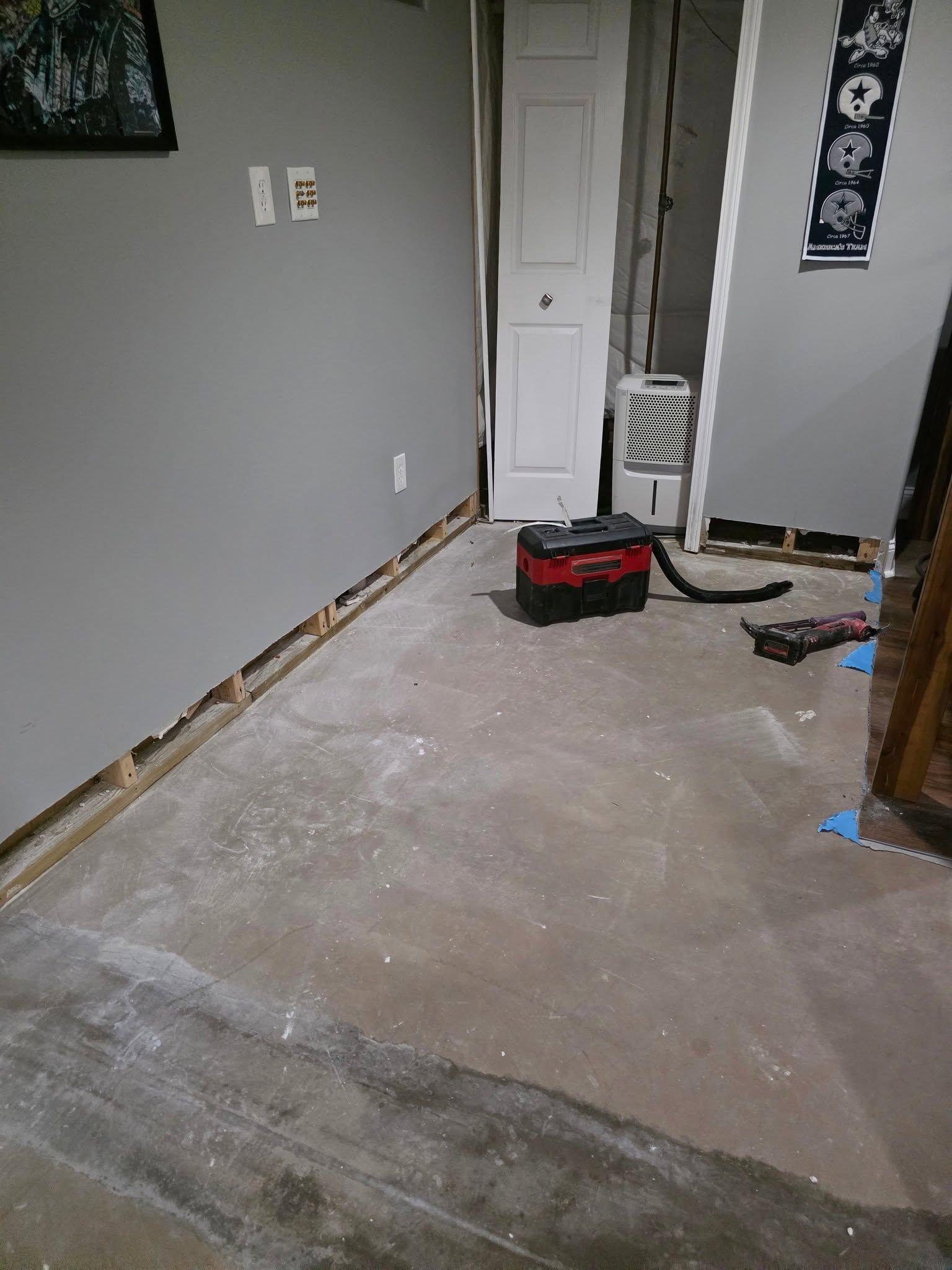 Partially stripped room with bare floor, gray walls, and tools near a closet door