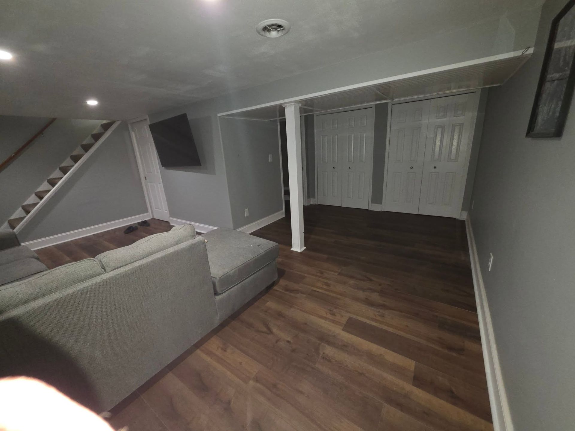 Basement living room with gray sectional sofa, staircase, and large closet doors.