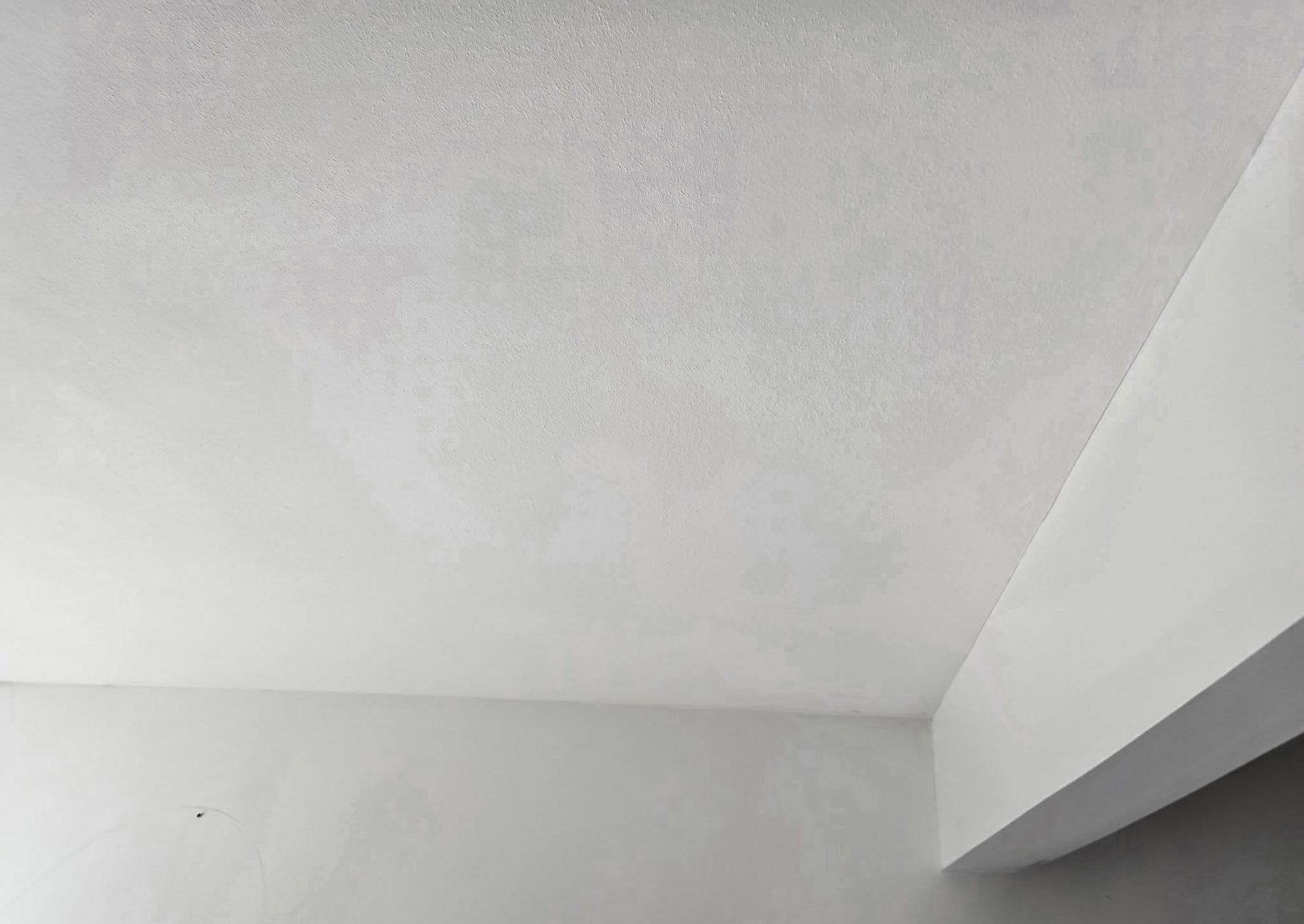 White ceiling and light gray walls meeting at a corner, with a slanted beam on the right.