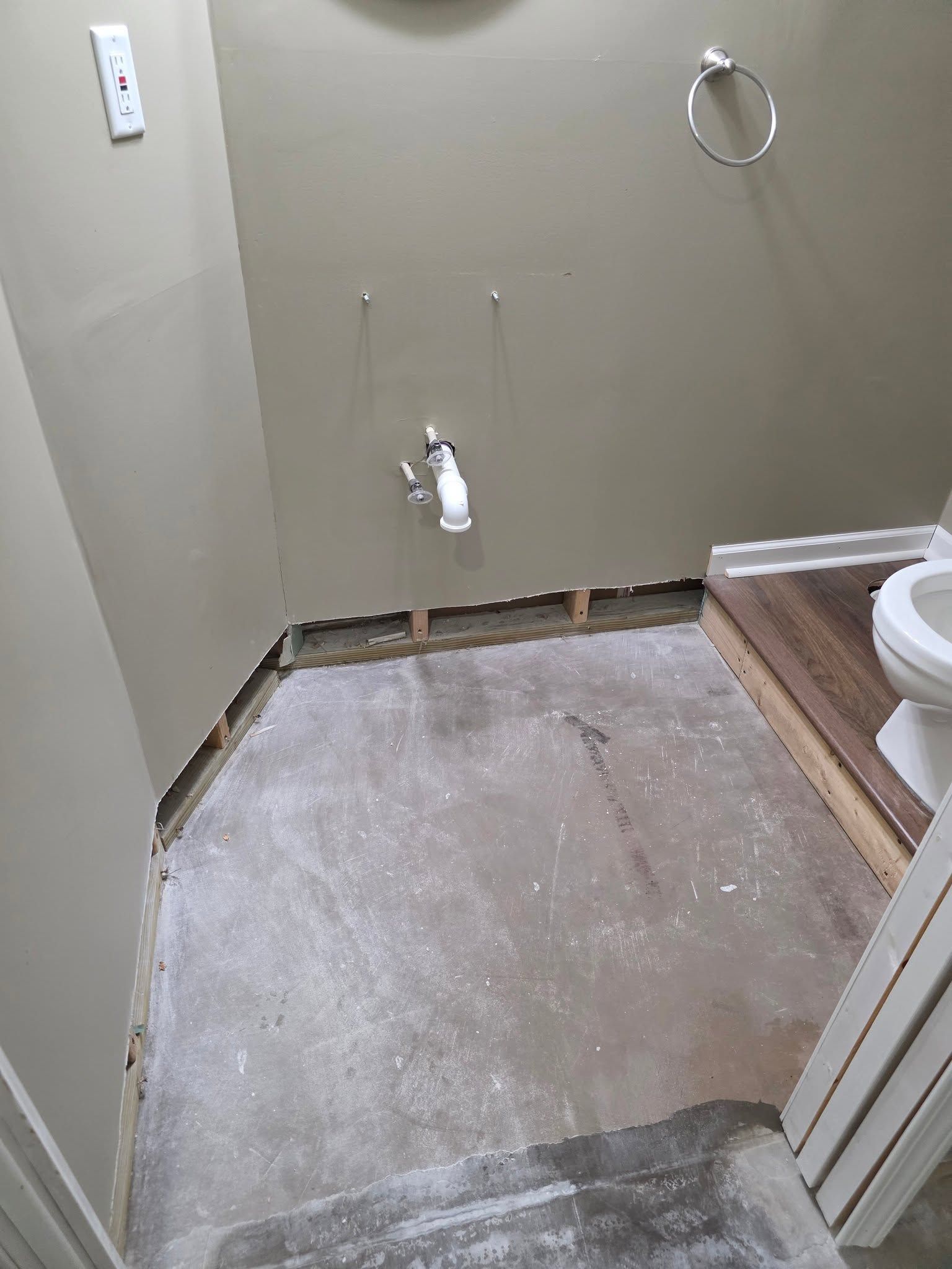 Small bathroom under renovation with exposed concrete floor and open plumbing under the sink.