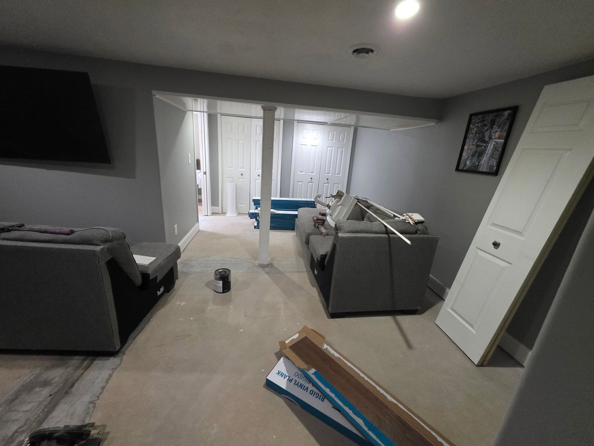 Dim living room with gray couches, TV, white door, and items scattered on the floor.