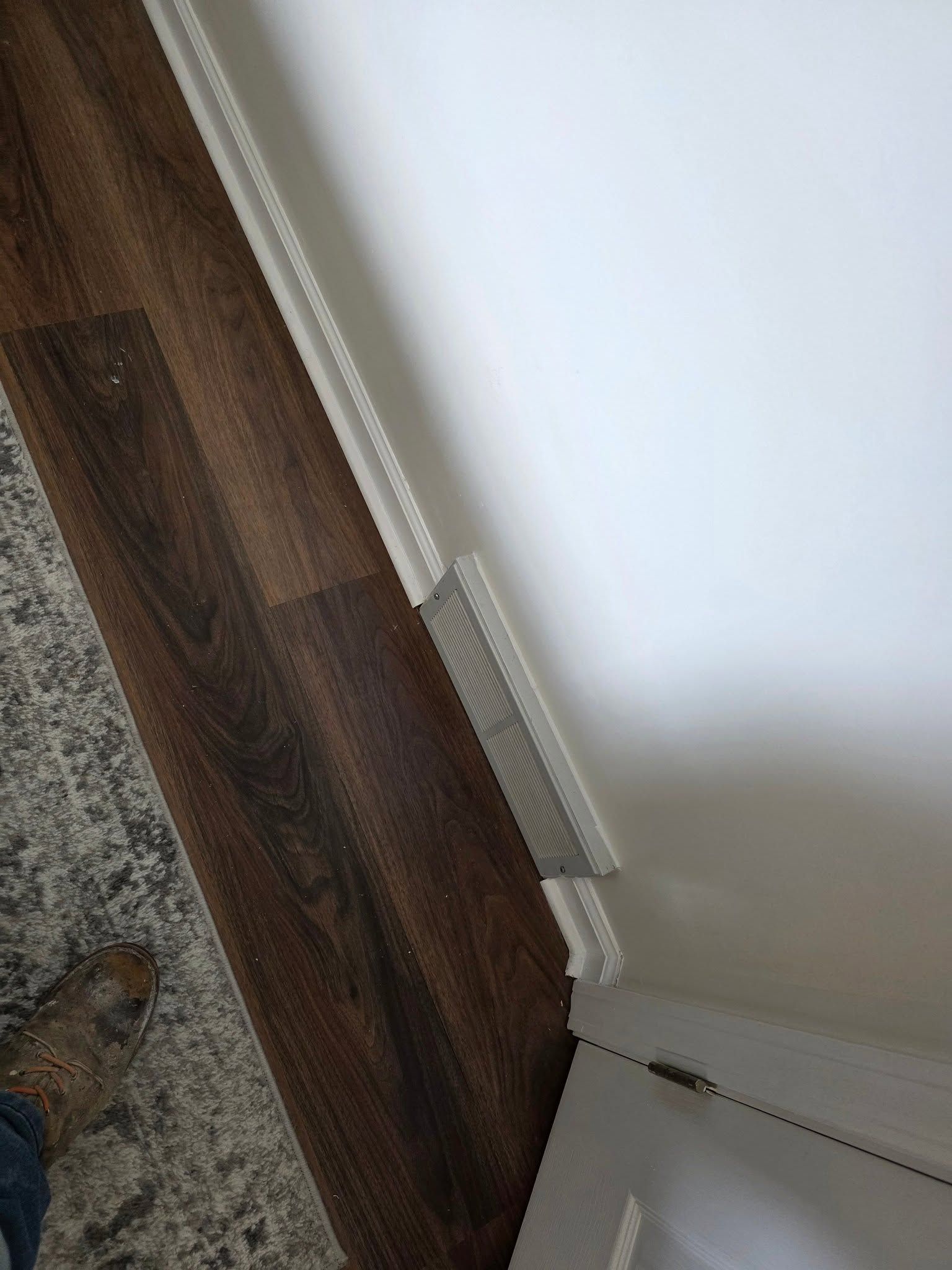 Corner of a room with white wall, brown wood floor, and a window blind hanging along the wall.
