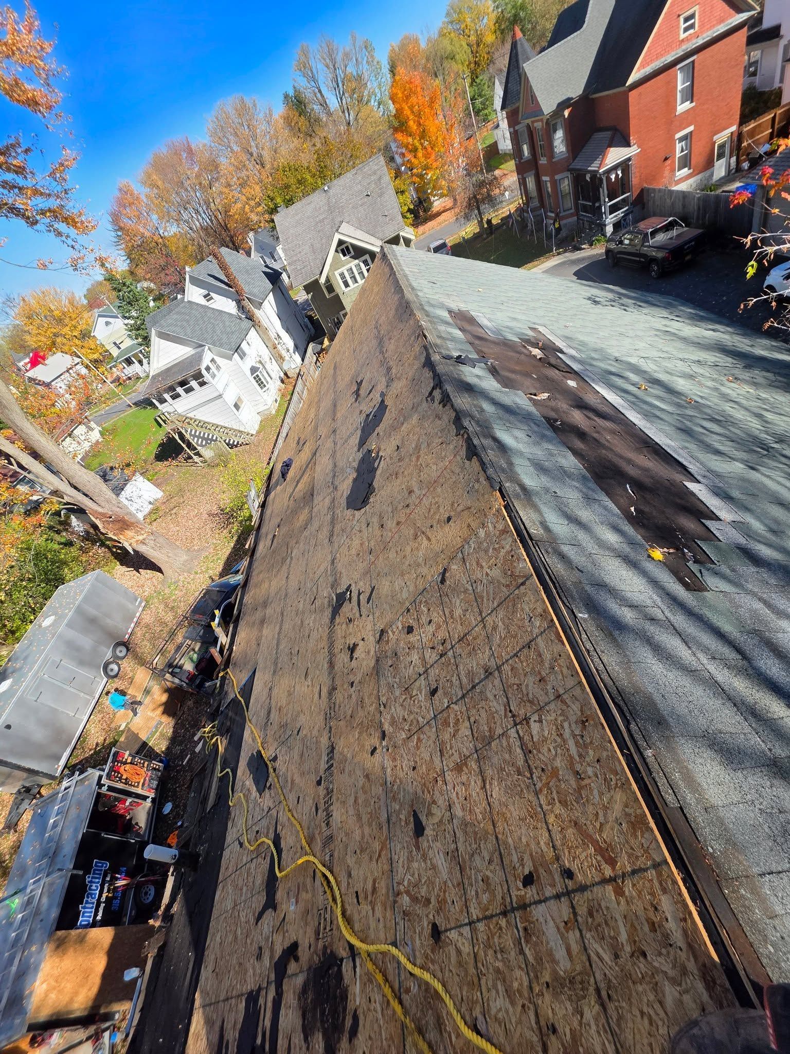 Steep shingled roof under repair beside brick buildings and autumn trees on a sunny day