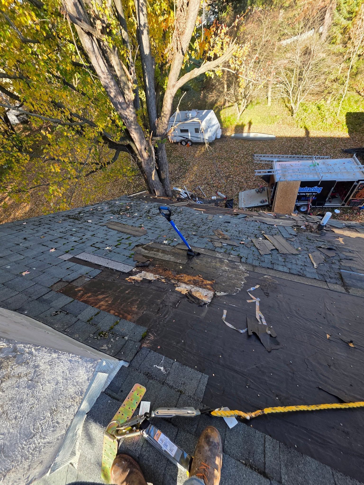 Rooftop repair area with damaged shingles, tools, and a ladder beside trees and a parked car below.
