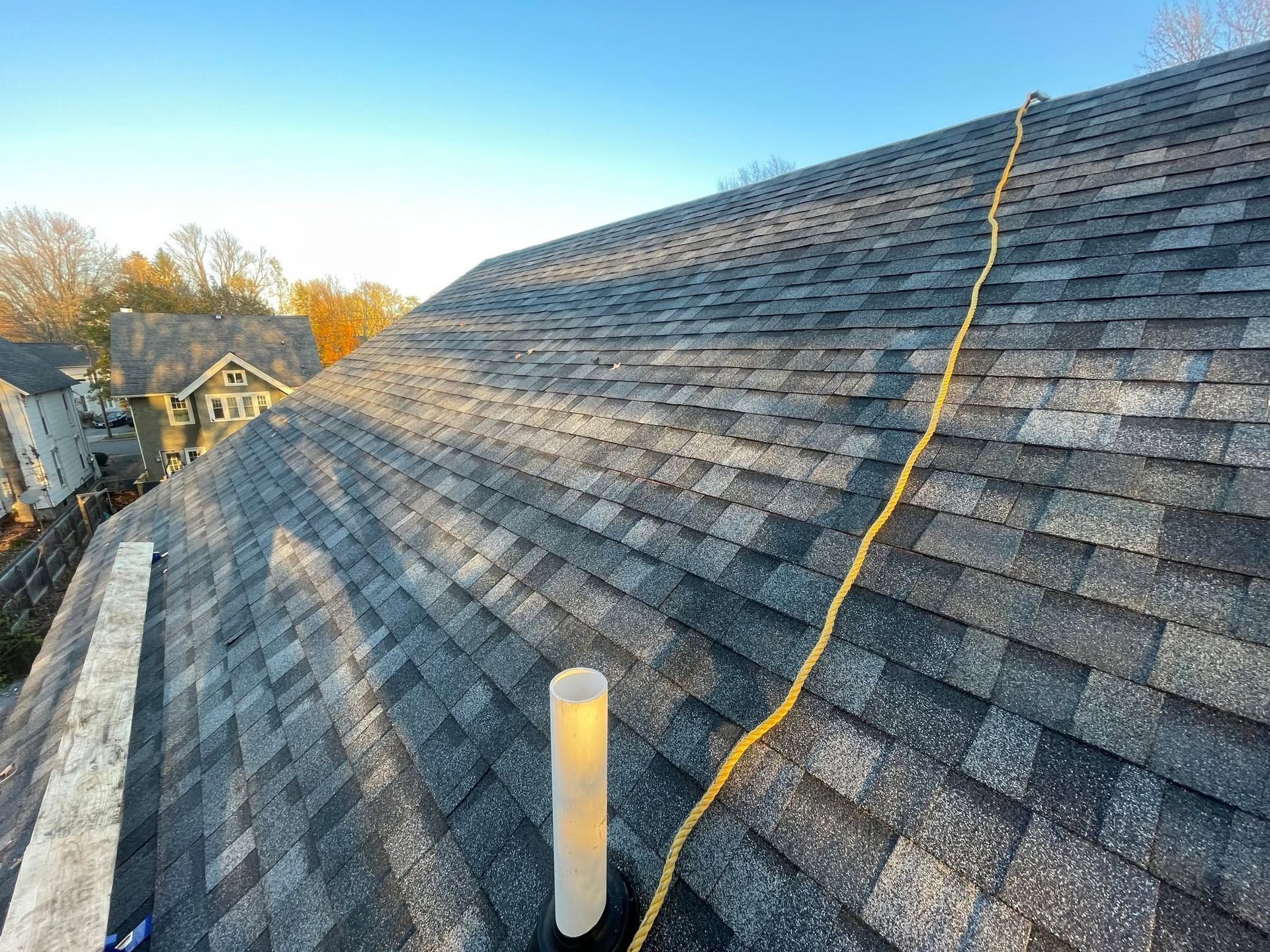 Steep gray shingle roof with a yellow rope running up it and a white vent pipe in the foreground