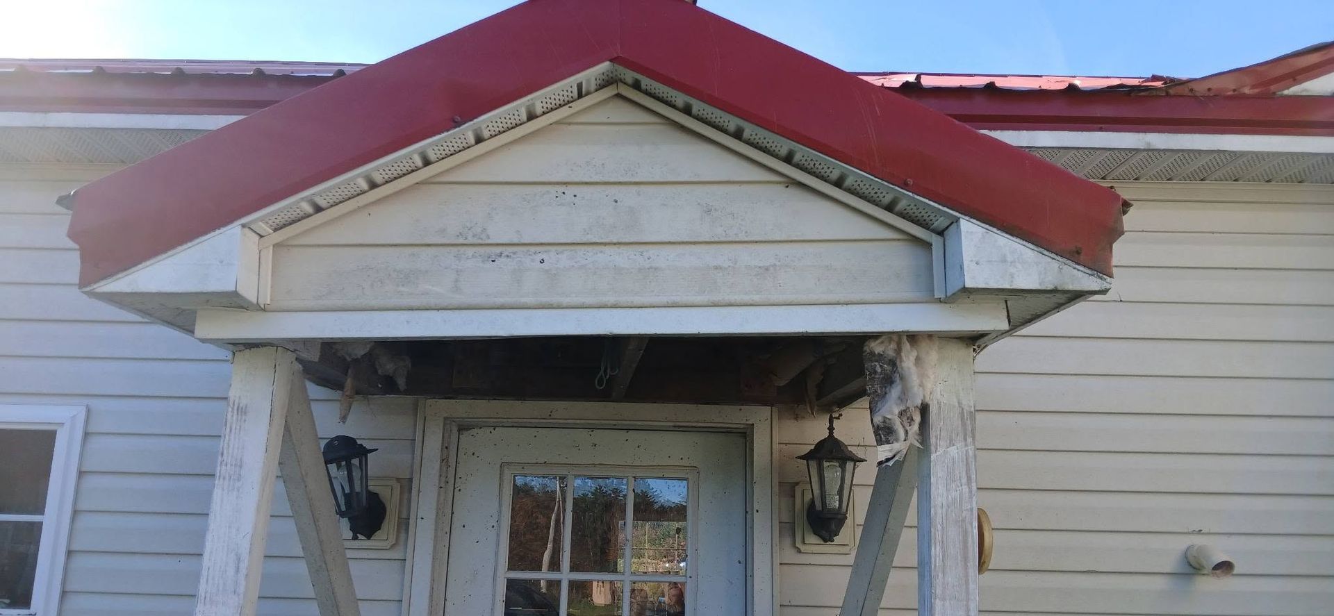 Damaged front porch with peeling white paint and a red roof over a doorway.
