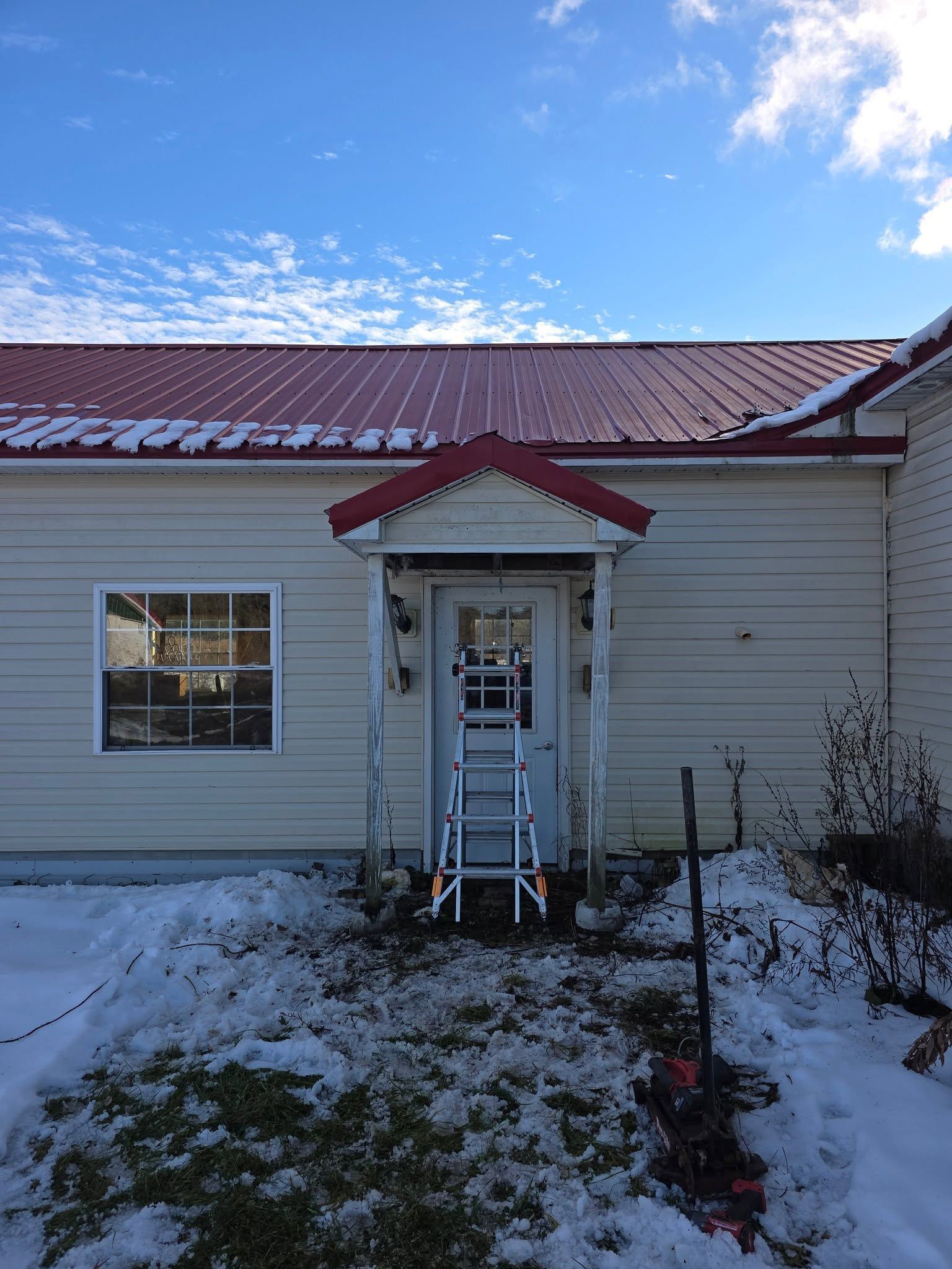 Snowy house exterior with a red metal roof and small white entry porch under a blue sky